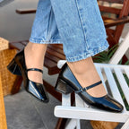 Person wearing black high-heeled shoes and blue jeans sitting on a chair.