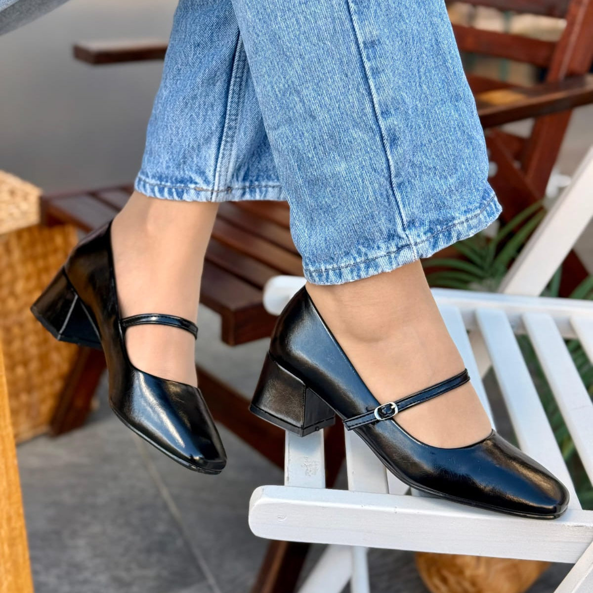 Person wearing black high-heeled shoes and blue jeans sitting on a chair.