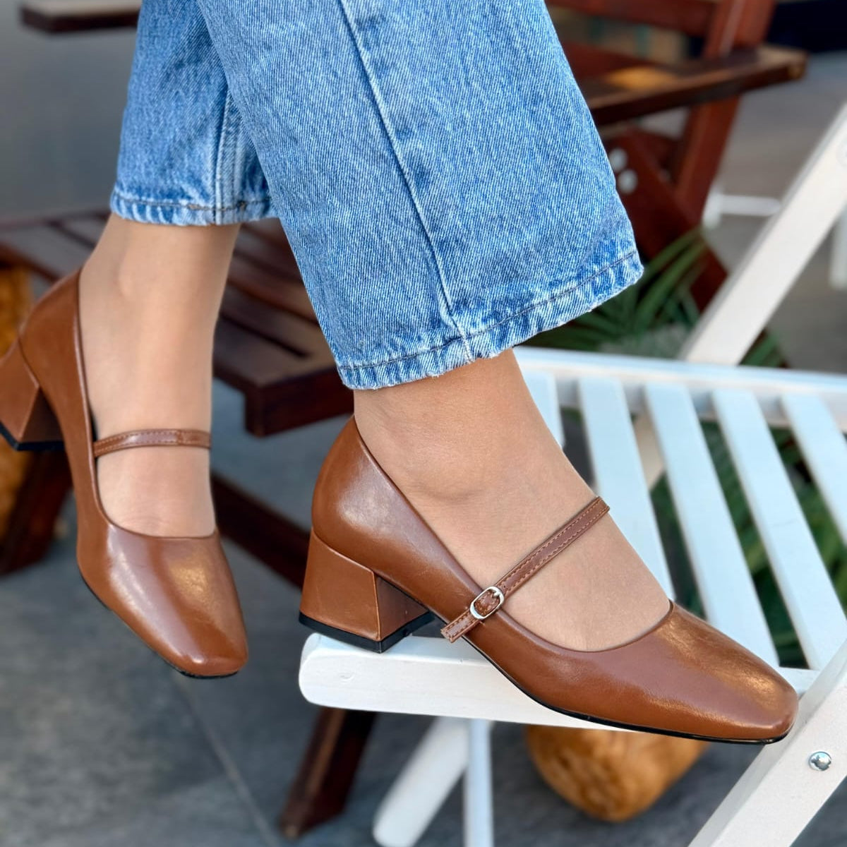 Brown shoes with a strap worn with blue jeans on a blurred outdoor background