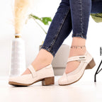 White shoes worn with blue jeans on a blurred indoor background, featuring the 'B Beautiful Comfort' brand.