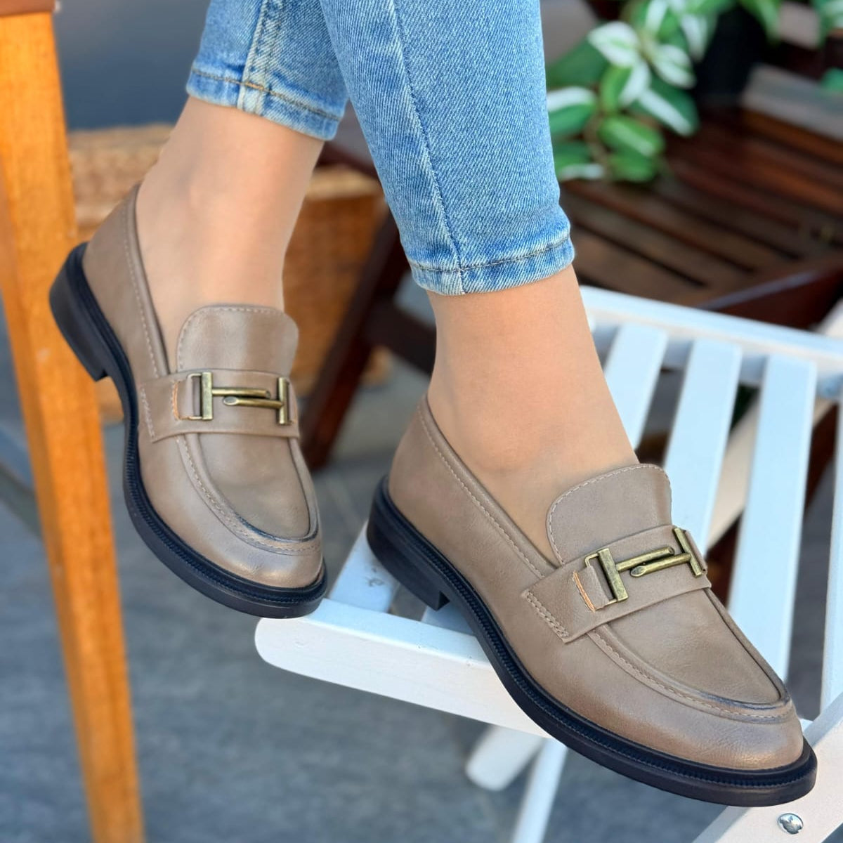 Beige loafers with gold accents worn by a person sitting on a chair.