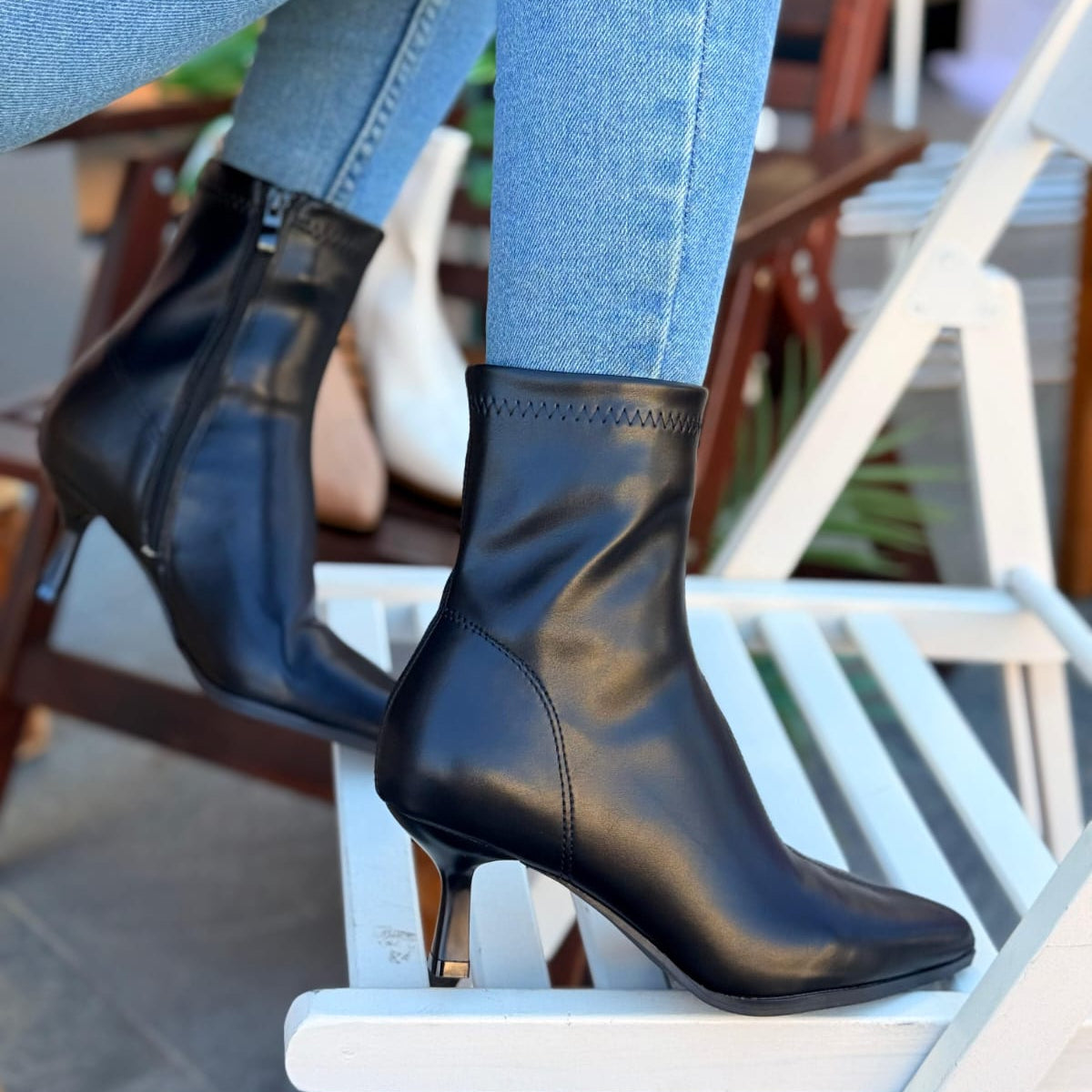 Black ankle boots worn with light blue jeans on a chair.