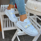 Light blue sneakers with gold accents worn by a person sitting on a chair.