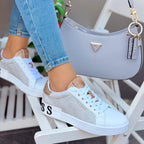 Person wearing white sneakers with brown accents, sitting on a white chair with a gray handbag in the background.