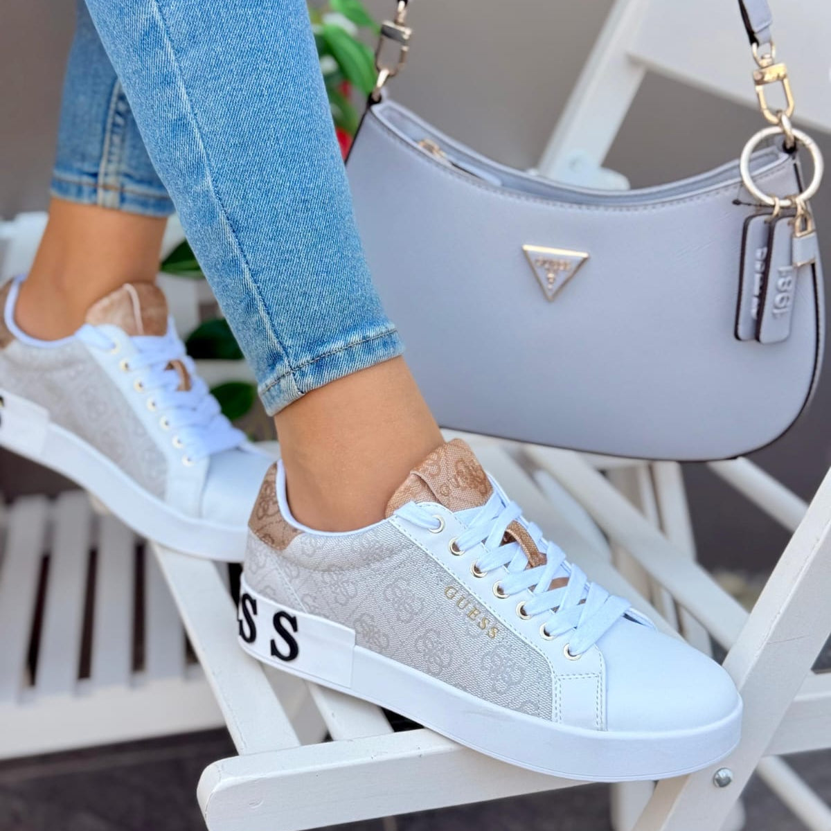Person wearing white sneakers with brown accents, sitting on a white chair with a gray handbag in the background.