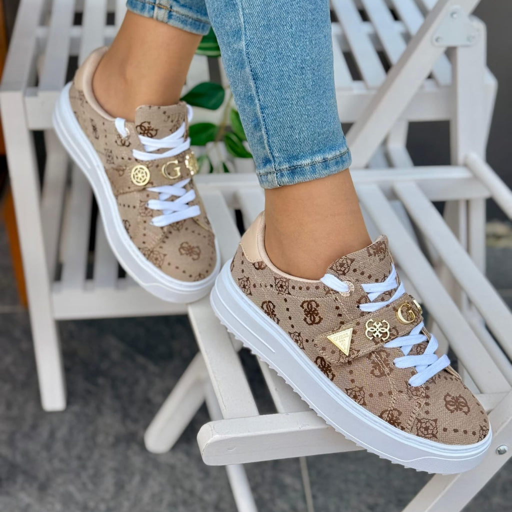 Beige patterned sneakers with white laces worn by a person sitting on a white chair.
