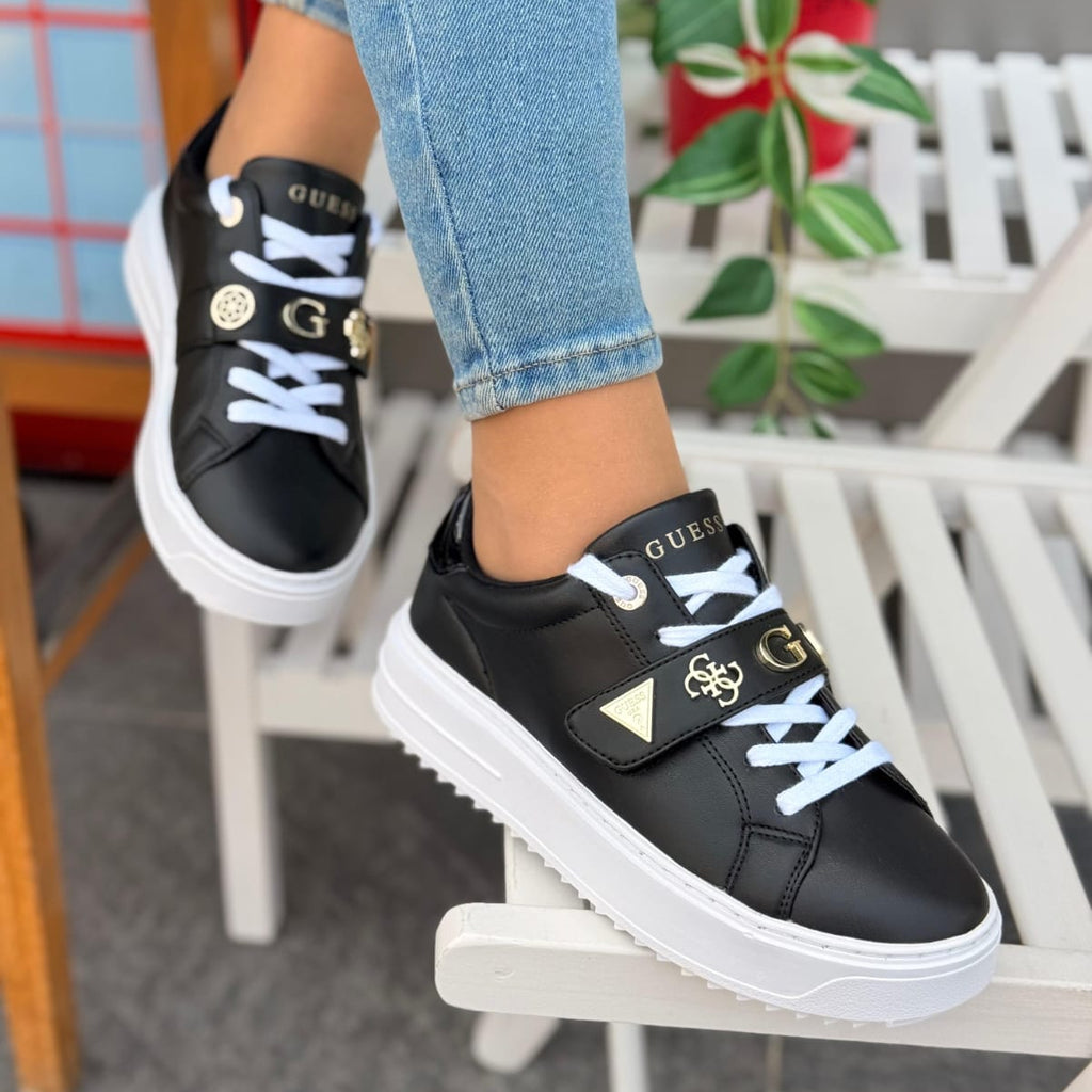 Black sneakers with white soles worn by a person sitting on a chair.