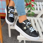 Black sneakers with white soles worn by a person sitting on a chair.