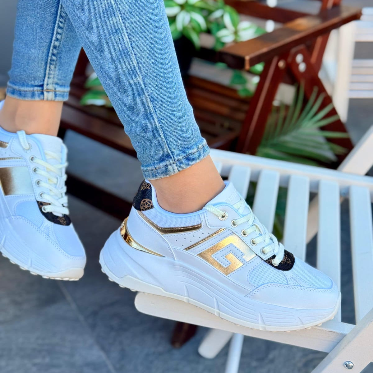 Light blue sneakers with gold accents worn by a person sitting outdoors.