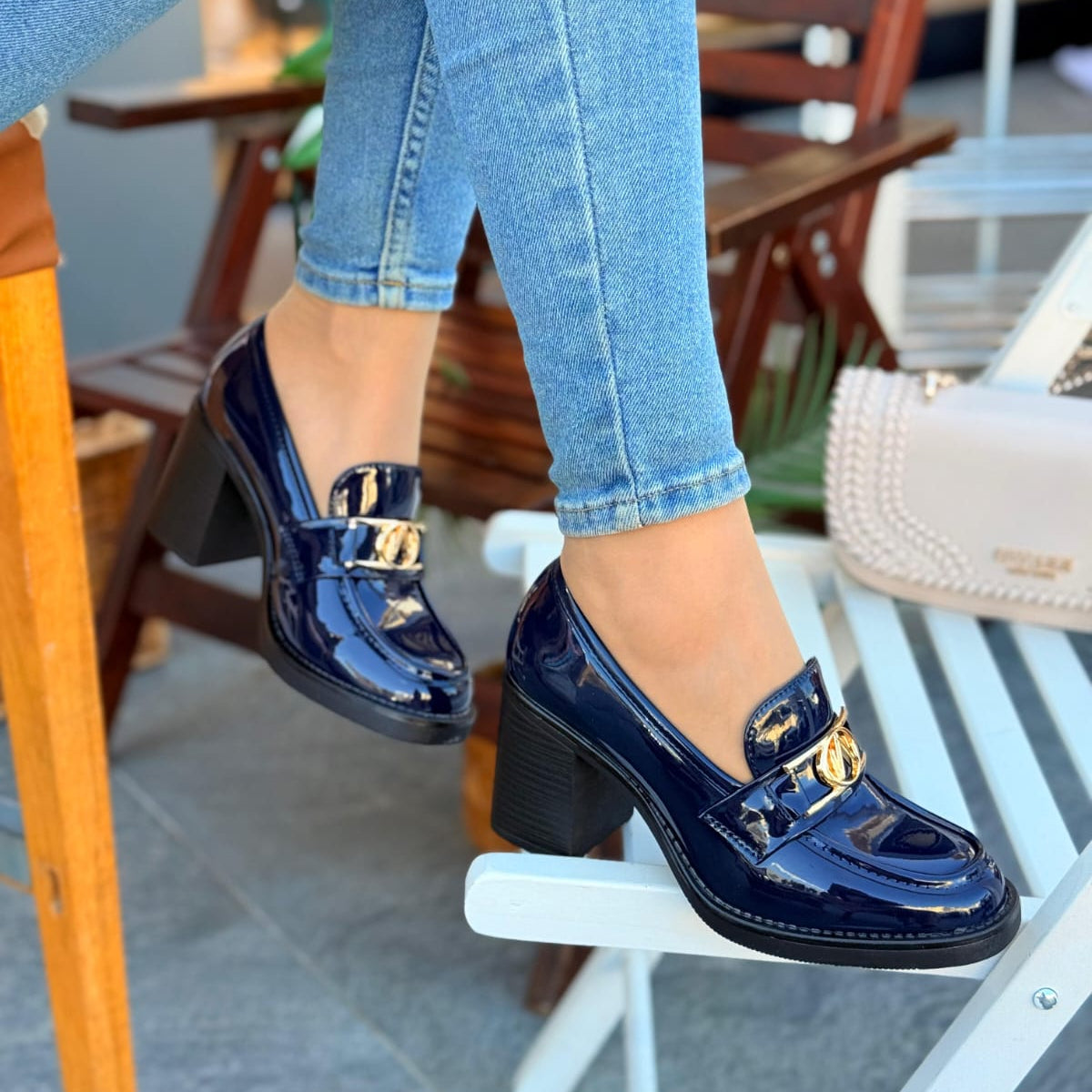 Person wearing blue patent leather shoes with gold buckles and jeans, sitting on a chair.