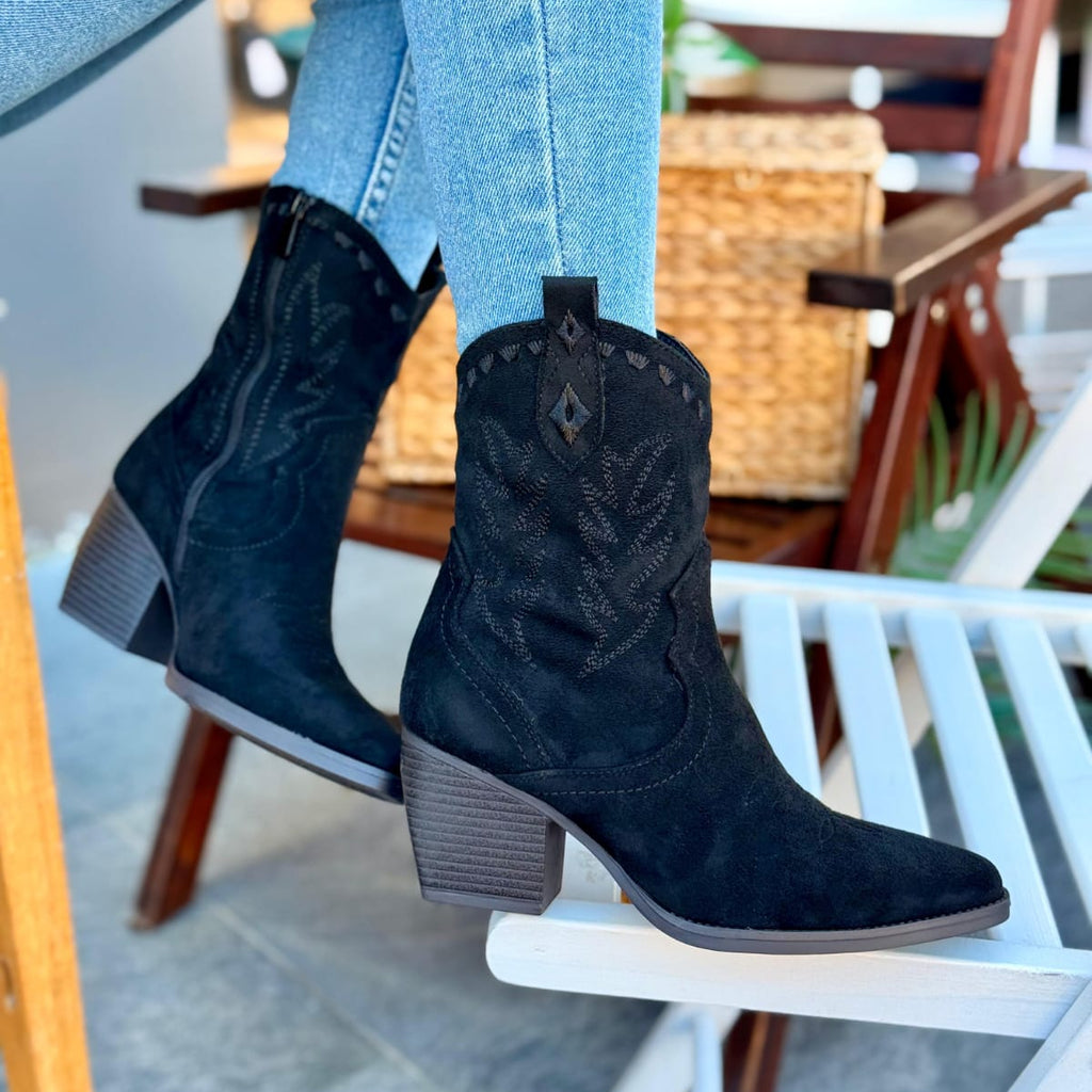 Black cowboy boots worn with light blue jeans on a chair.