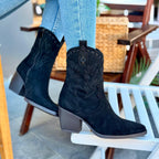 Black cowboy boots worn with light blue jeans on a chair.
