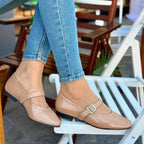 Person wearing beige flat shoes with a strap, standing on a chair indoors.
