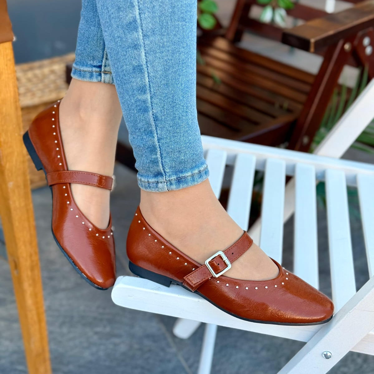 Brown shoes with buckles worn by a person sitting on a white chair.