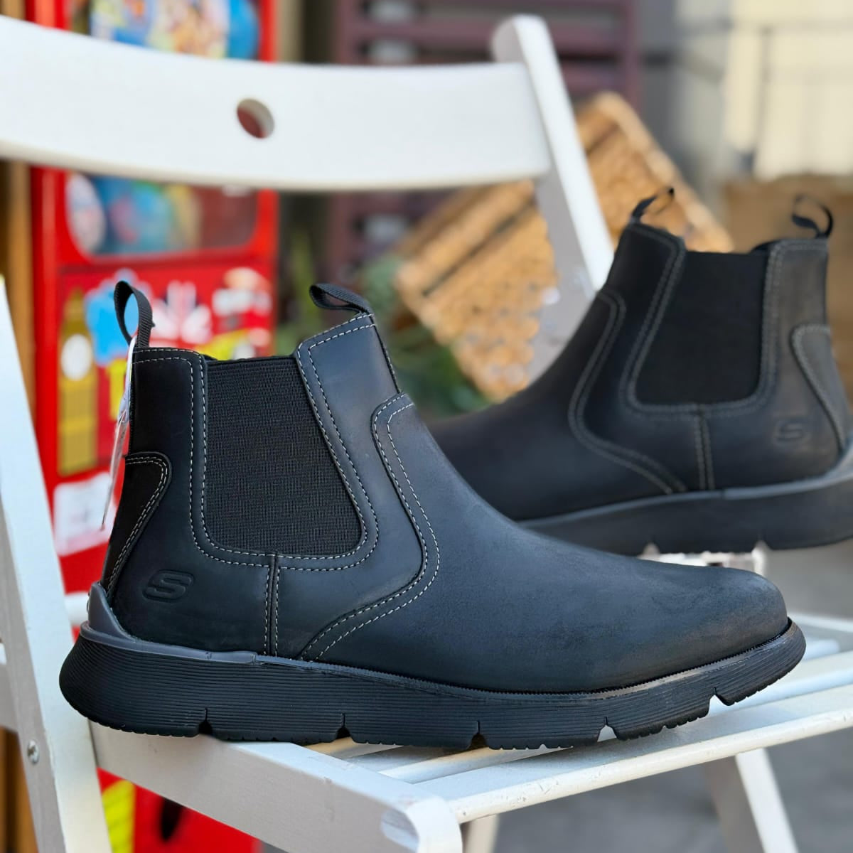 Pair of Skechers Augustino Paulo black leather men’s boots displayed outdoors on a white chair.