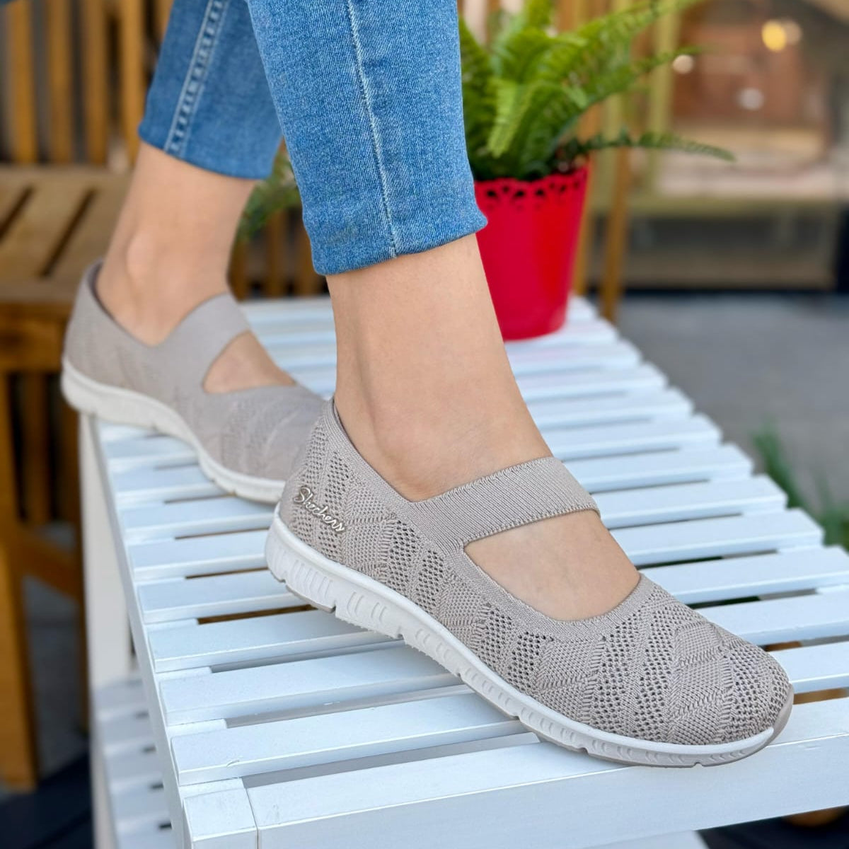 Woman wearing Skechers Be-Cool Sweet Knit beige Mary Jane flats sitting outdoors on a white chair.