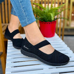 Woman wearing Skechers Be-Cool Sweet Knit balck Mary Jane flats sitting outdoors on a white chair.