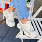 Woman wearing Skechers D'Lites 5.0 Team beige chunky sneakers with white and grey sole.