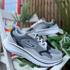 Pair of Skechers GOrun Consistent 2.0 men’s gray sneakers displayed outdoors with plants in background.