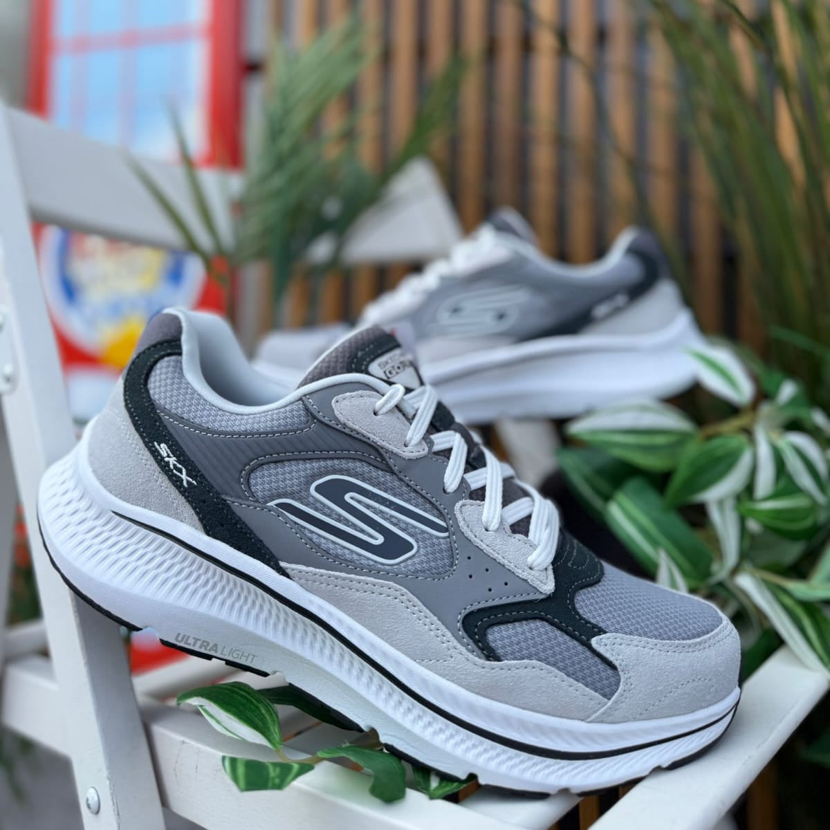 Pair of Skechers GOrun Consistent 2.0 men’s gray sneakers displayed outdoors with plants in background.
