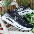 Pair of Skechers GOrun Max Cushioning Propulsion black running shoes displayed outdoors with plants in background.