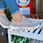 Woman wearing Skechers Glide-Step Pro beige slip-ins with geometric sole design sitting outdoors.