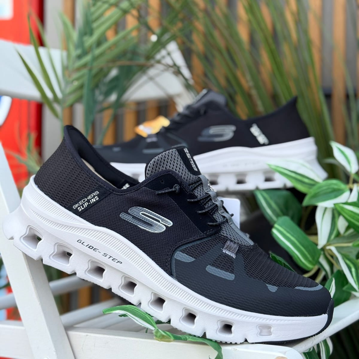 Pair of Skechers Slip-Ins Glide-Step Pro men’s black sneakers displayed outdoors with plants in background.