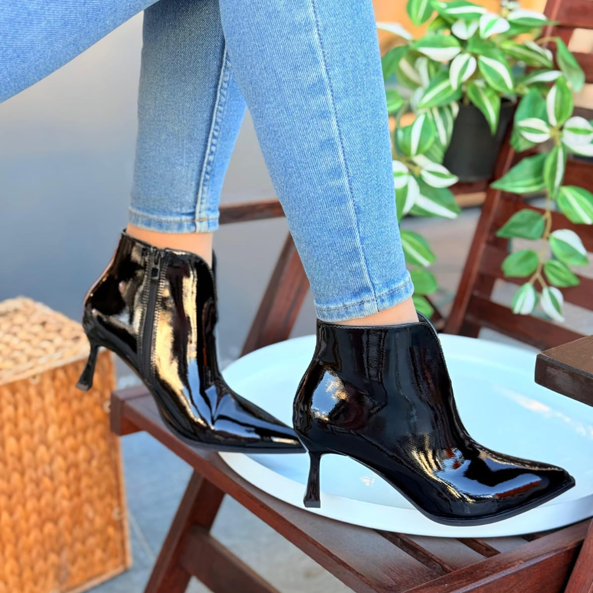 Black patent high-heeled shoes worn with light blue jeans on a chair.