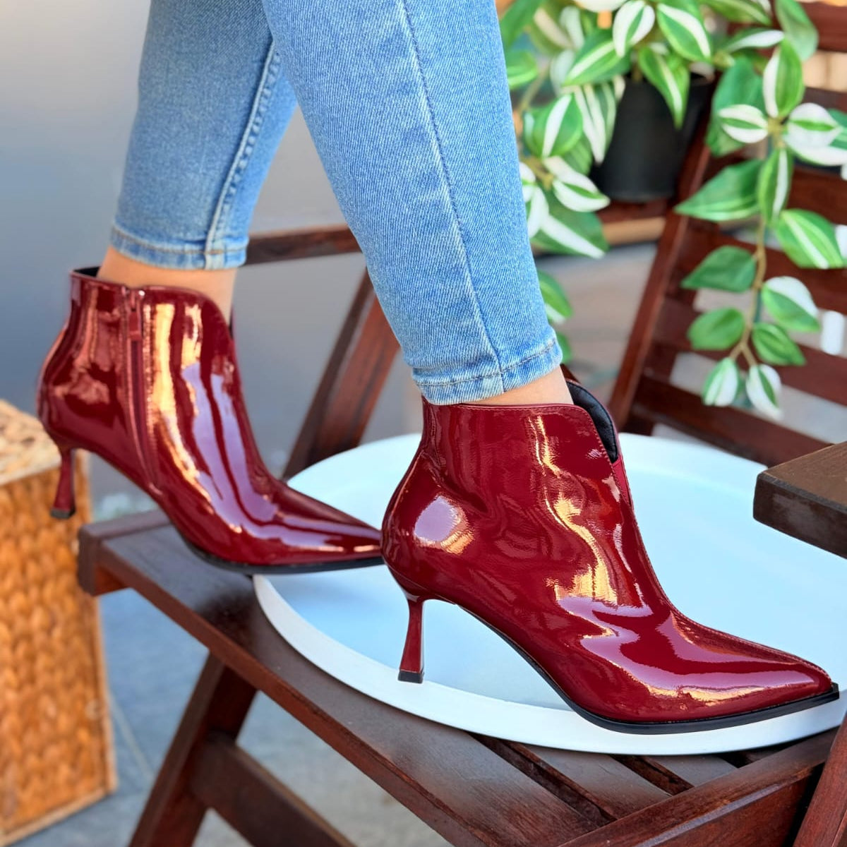 Red patent leather high-heeled boots worn with light blue jeans on a chair.