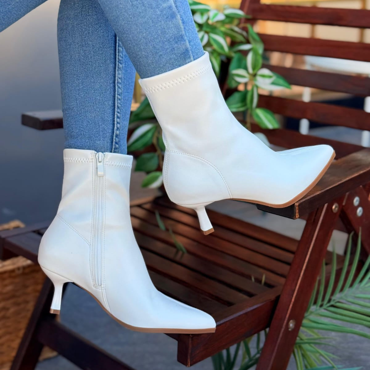 White ankle boots worn with blue jeans on a wooden chair.