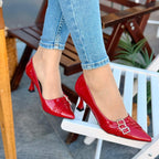 Red high-heeled shoes worn with light blue jeans on a blurred outdoor background