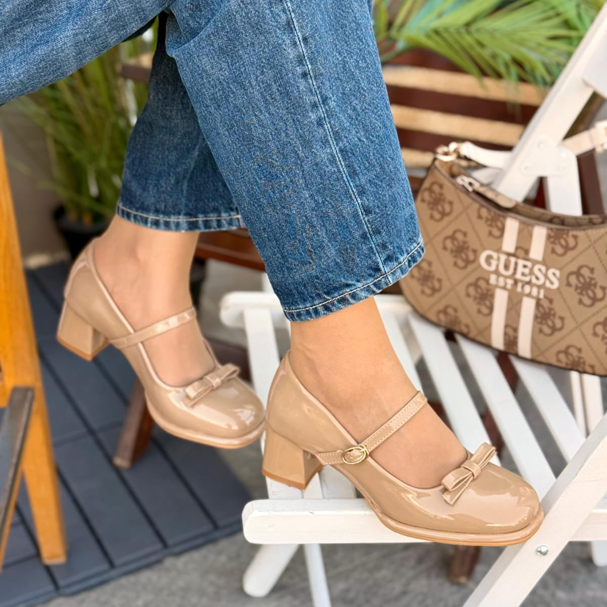 Person wearing beige shoes with a bow, sitting on a chair with a Guess bag in the background.