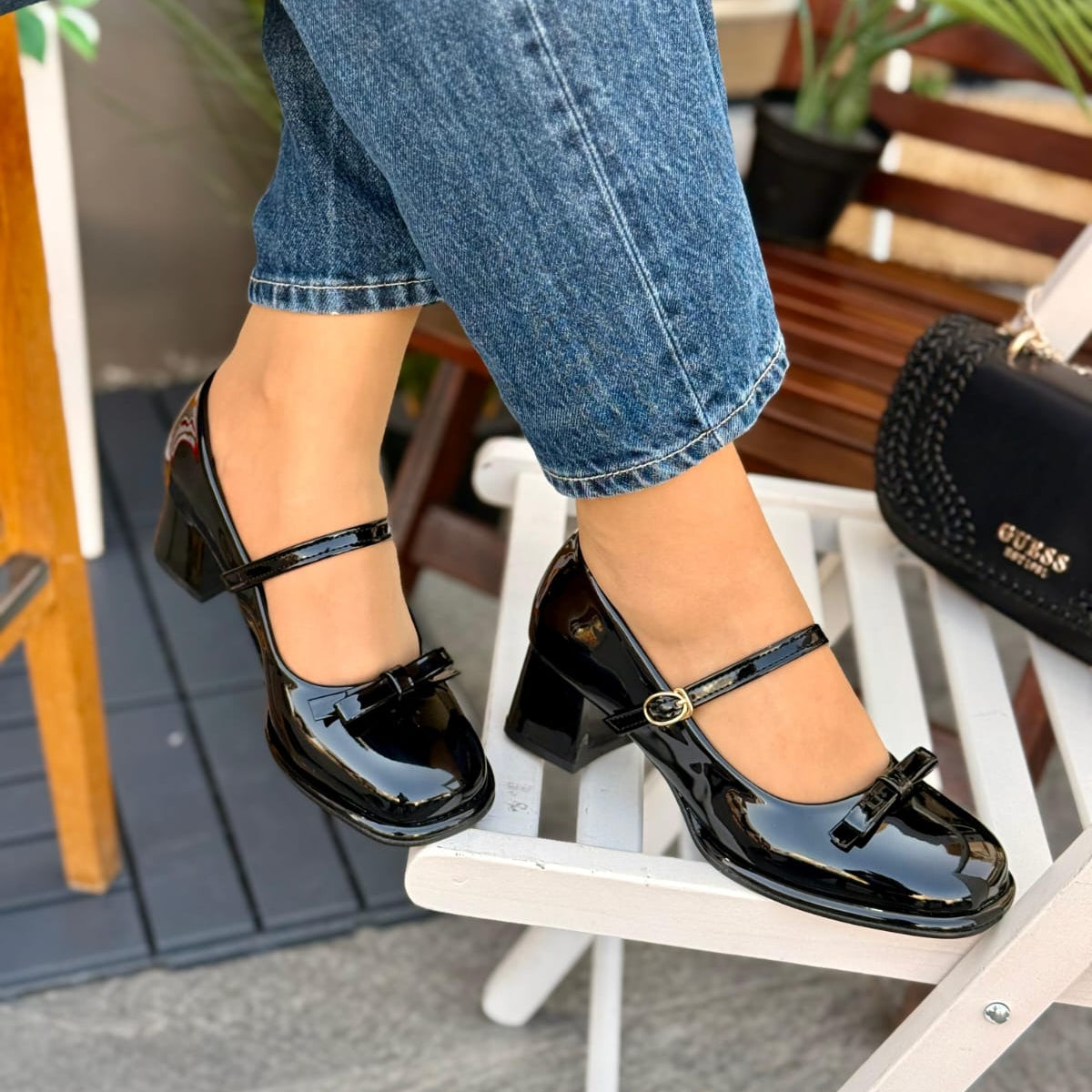 Black patent leather shoes worn with blue jeans on a chair.
