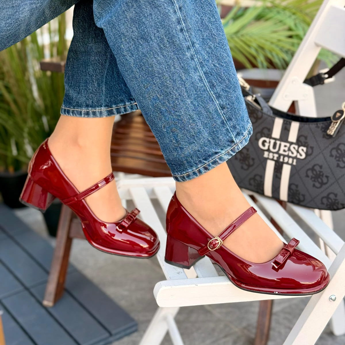 Red patent leather shoes worn with blue jeans, sitting on a white chair.