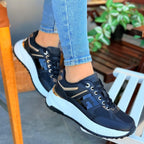 black sneakers with gold accents worn by a person sitting on a chair.