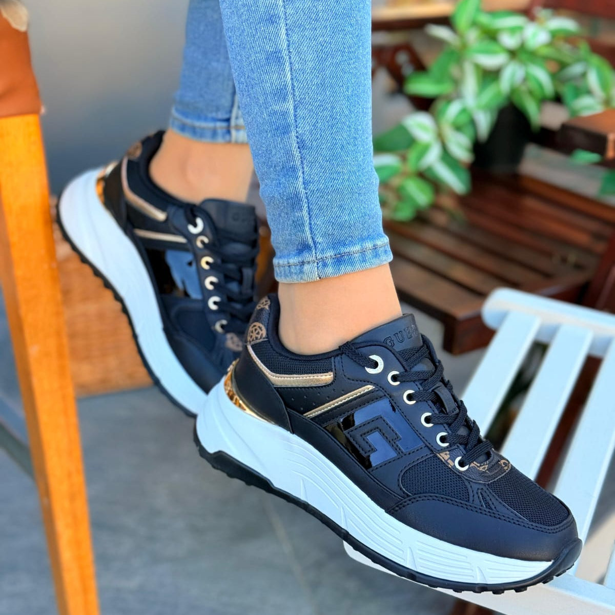 black sneakers with gold accents worn by a person sitting on a chair.