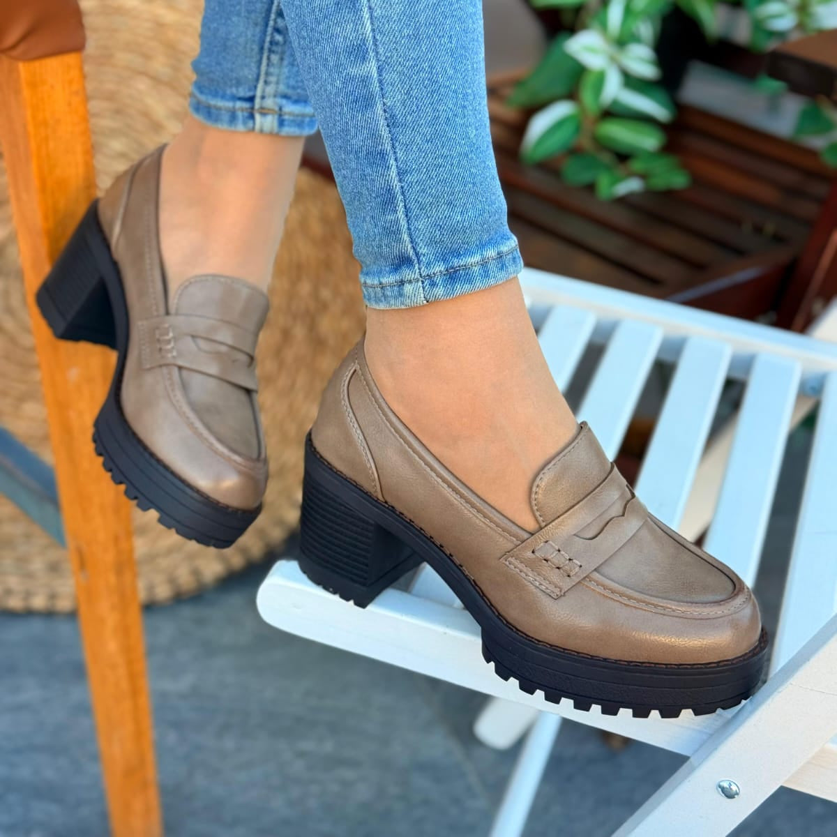 Person wearing beige loafers with thick black soles on a chair.