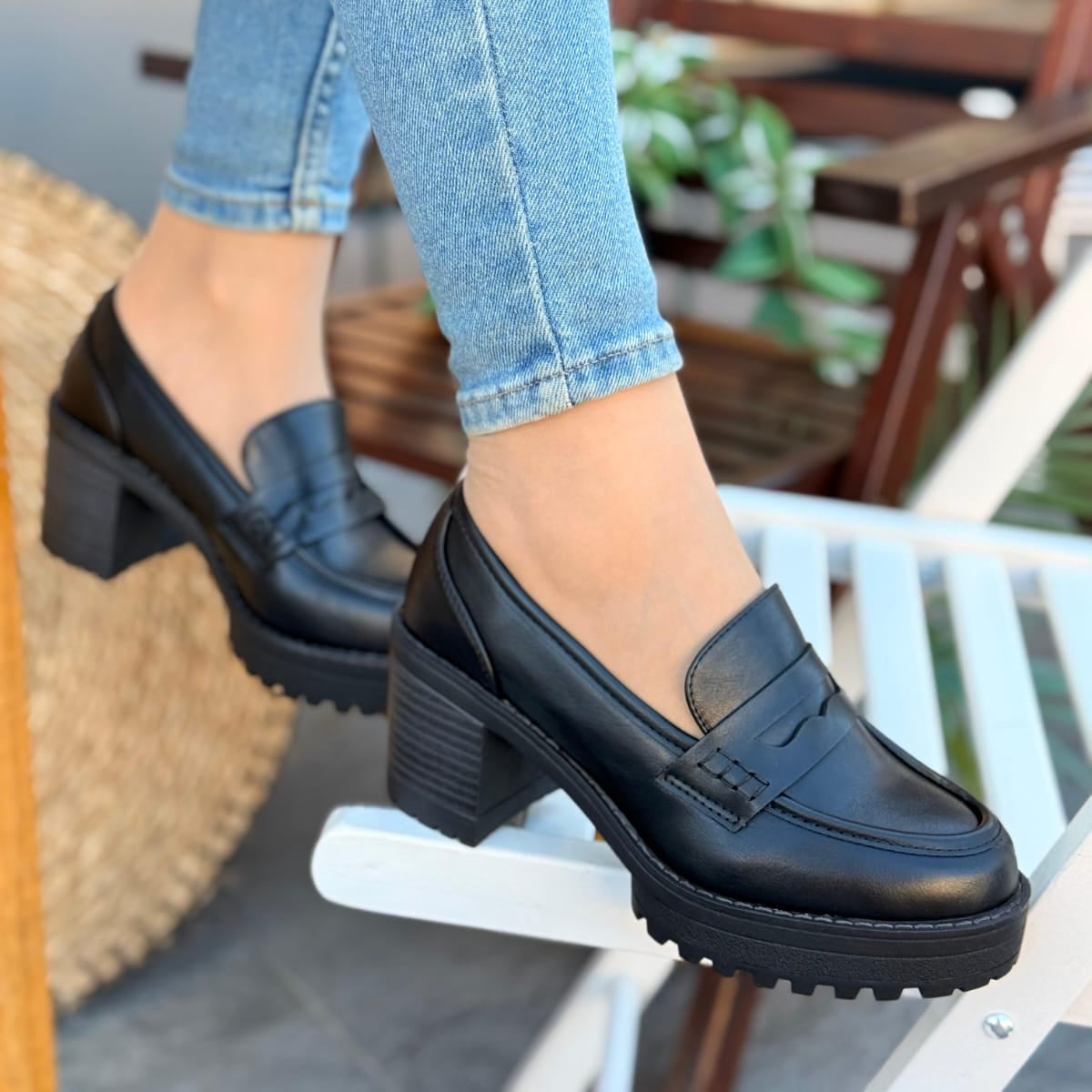 Black loafers worn with light blue jeans on a blurred outdoor background