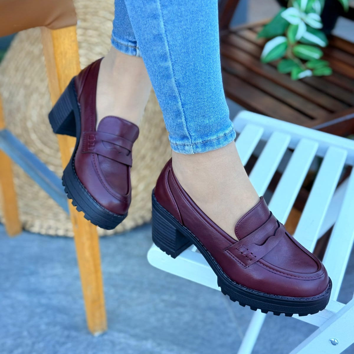 Burgundy loafers worn with blue jeans on a blurred indoor background