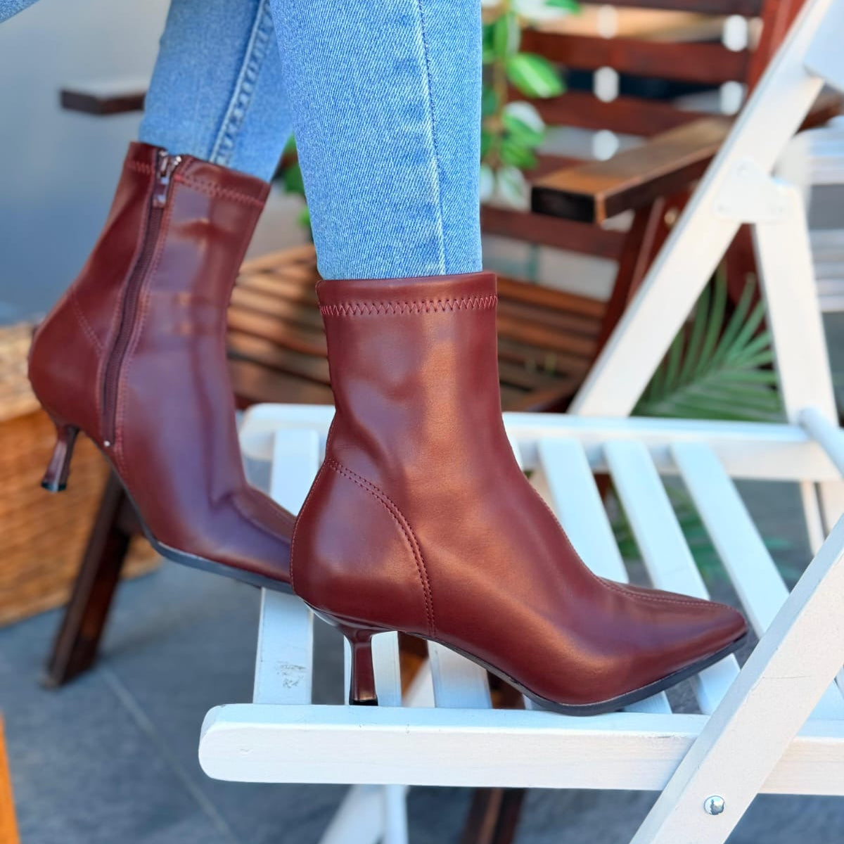 red leather boots worn with light blue jeans on a white chair.