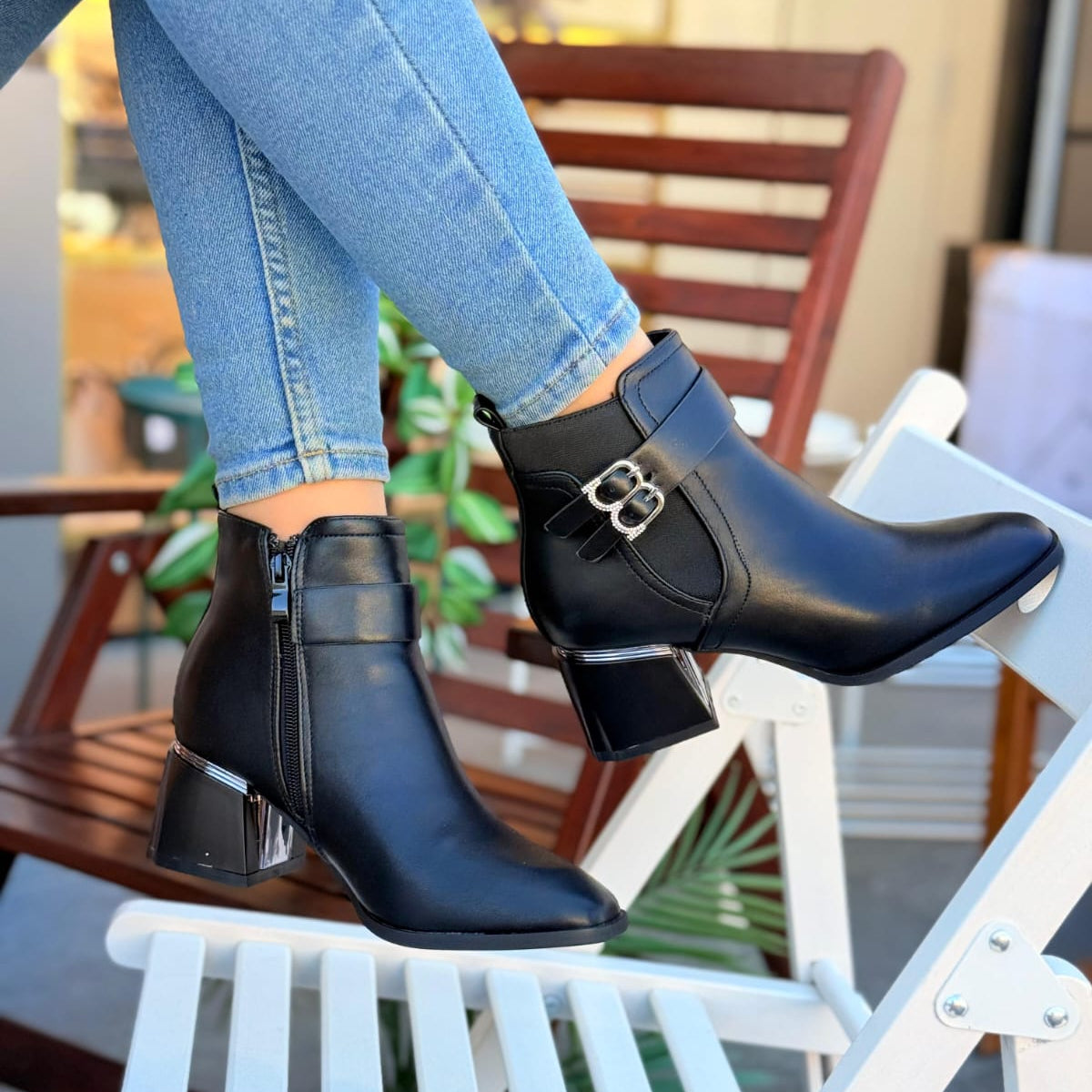 Black ankle boots with a metallic buckle worn by a person sitting on a chair.