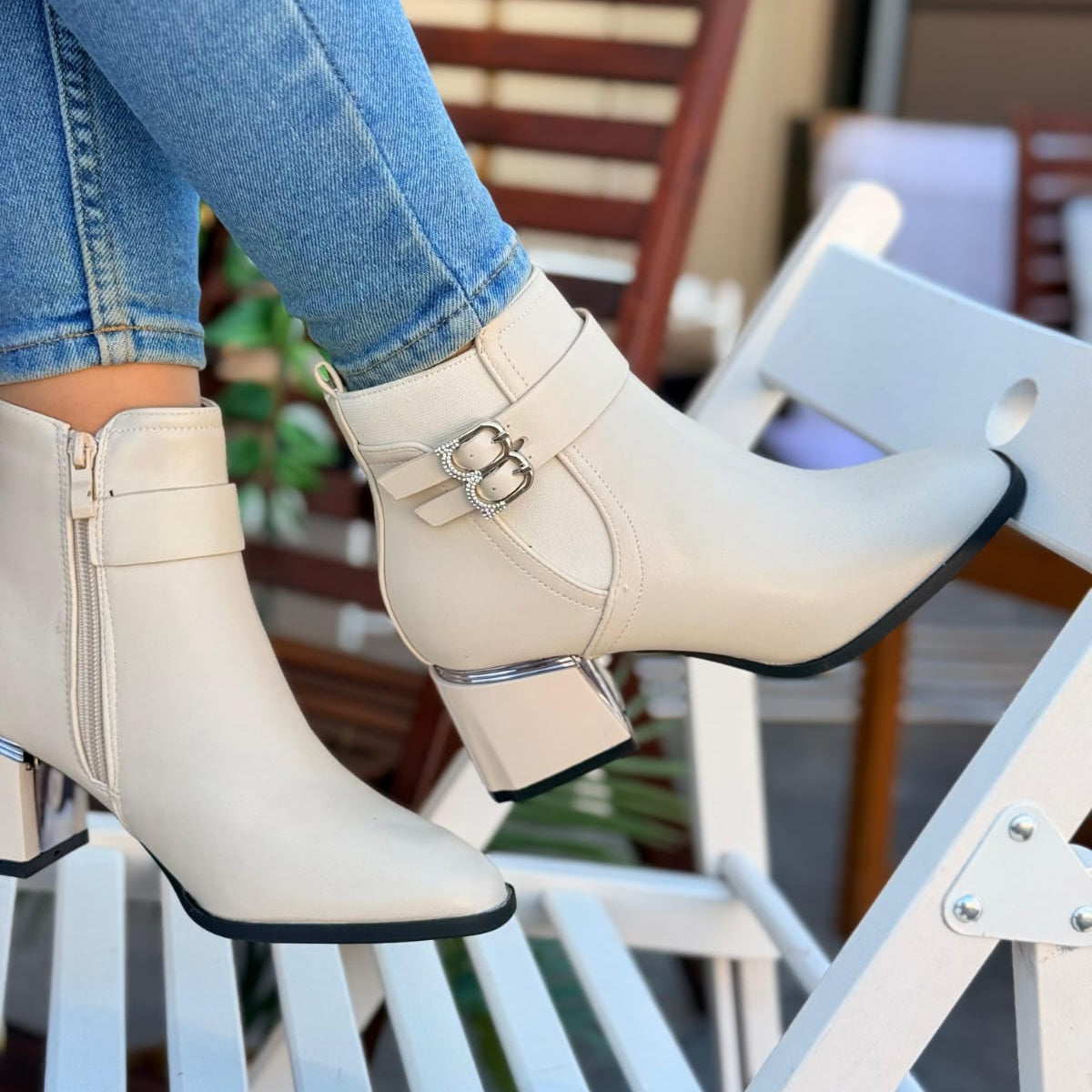 White ankle boots with a buckle detail worn by a person sitting on a chair.