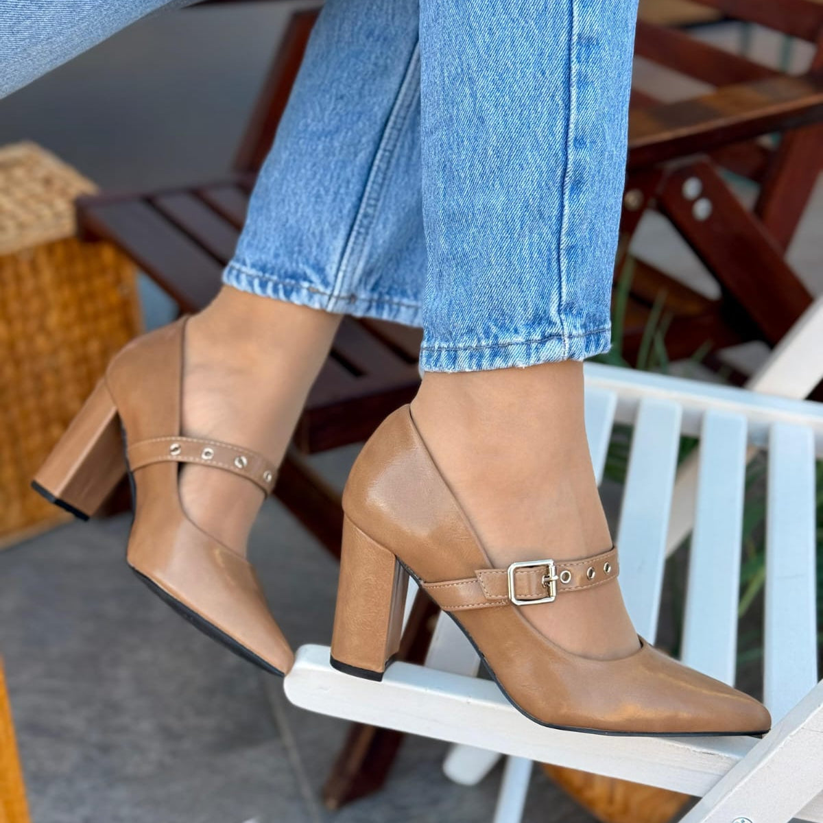 Tan high-heeled shoes with buckles worn with blue jeans on a chair.