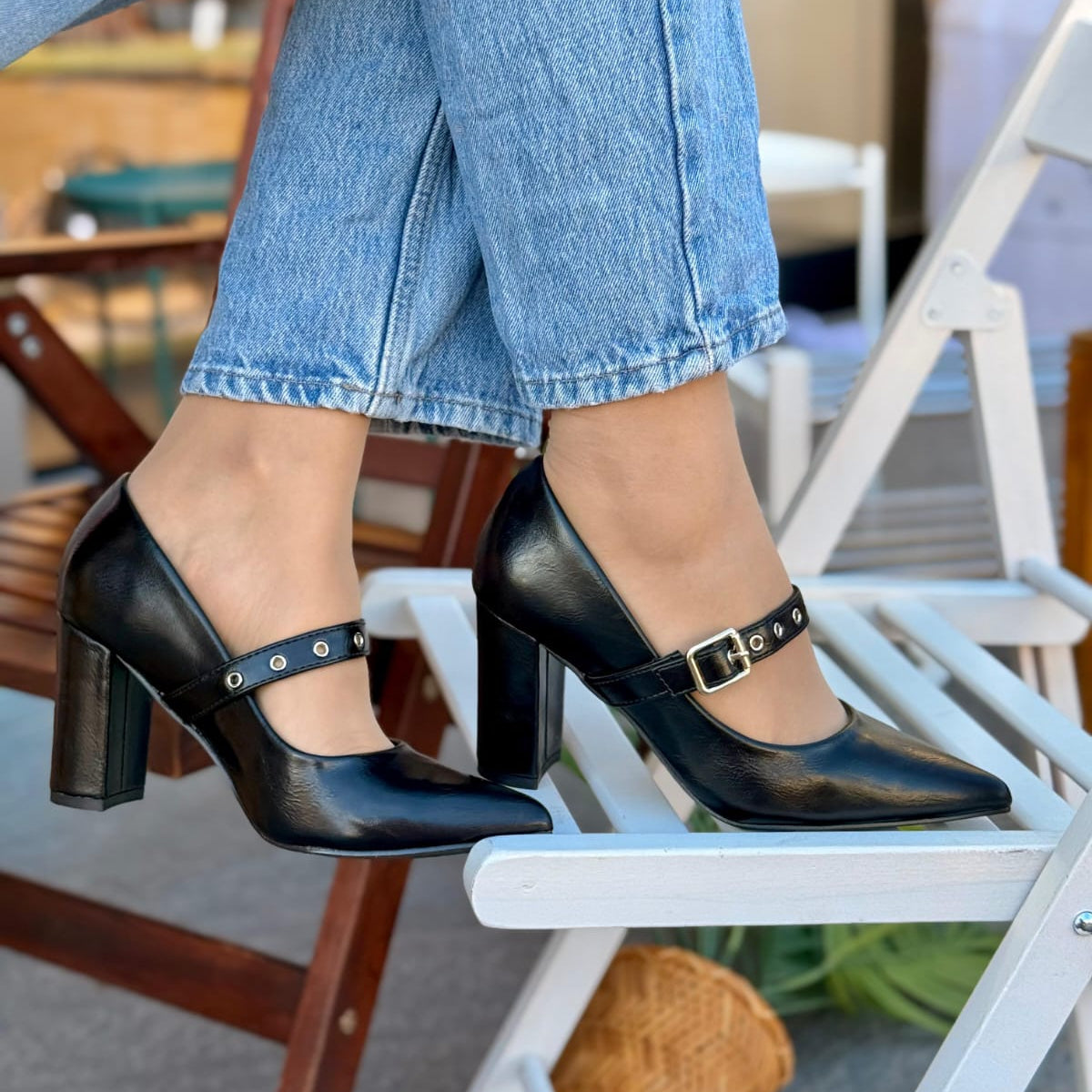 Person wearing black high-heeled shoes with buckles sitting on a chair.