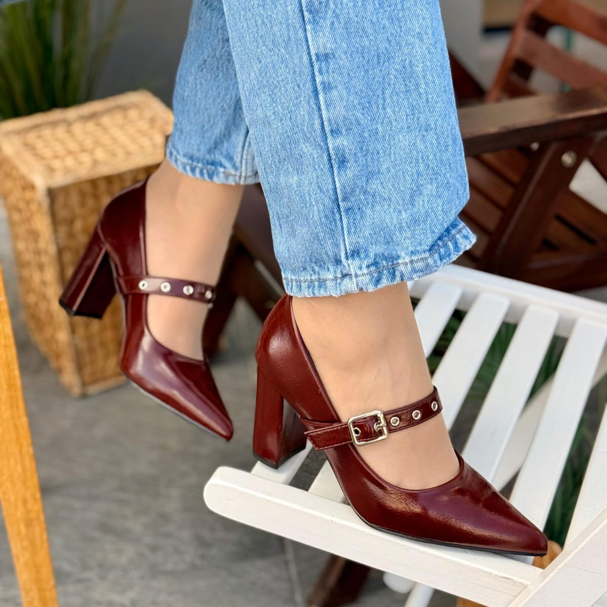 Red high-heeled shoes with strap worn by a person in light blue jeans, sitting on a white chair.